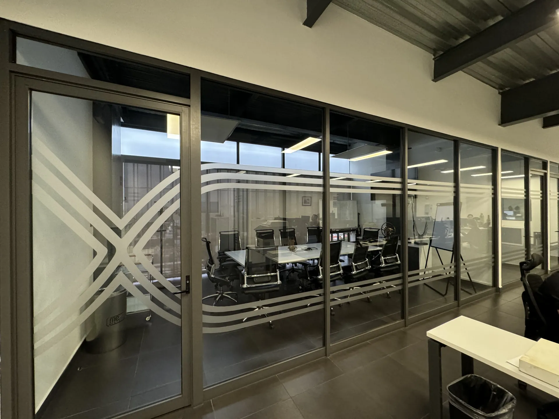 Pasillo de oficina con divisiones de cristal y película decorativa con franjas esmeriladas.