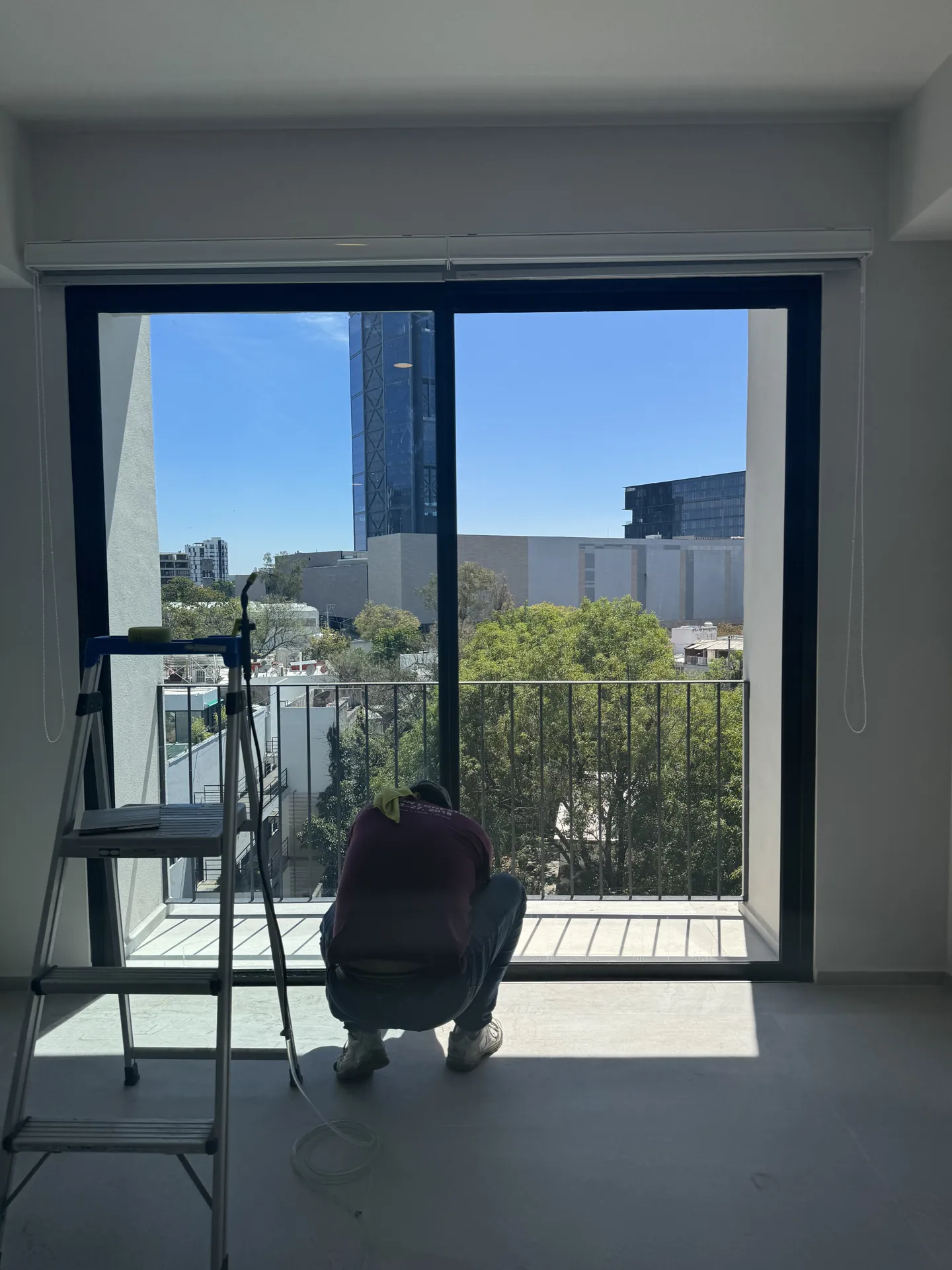 Instalador de espaldas aplicando película en el cancel de balcón de un departamento con vista urbana.